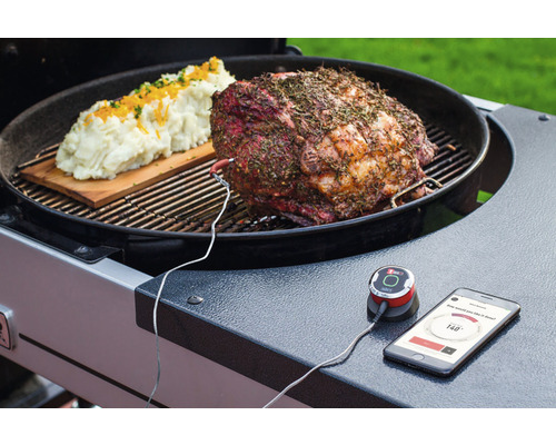 Een braadstuk en aardappelpuree op een grill met een aangesloten thermometer en een smartphone die de temperatuur weergeeft.