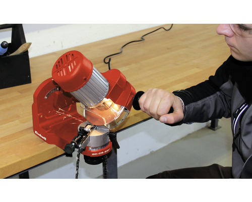 Een man slijpt een kettingzaag met een kettingzaagslijper van het merk Einhell.