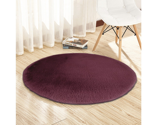 Rond, hoogpolig tapijt op houten vloer met stoel en boeken op de achtergrond.