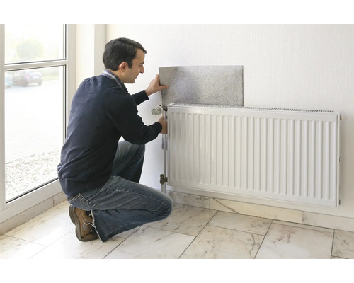 Man monteert een radiatorfolie achter een radiator aan een muur