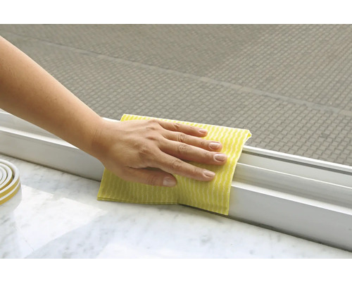 Een persoon maakt een raamkozijn schoon met een doek.