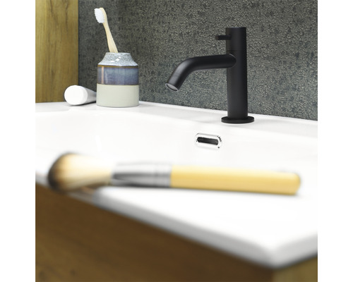 Zwarte wastafelmengkraan op een witte wastafel met tandenborstel, tandpasta en make-up kwast