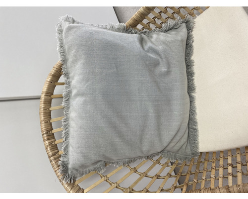 Vierkant kussen met franjes op een rotan stoel