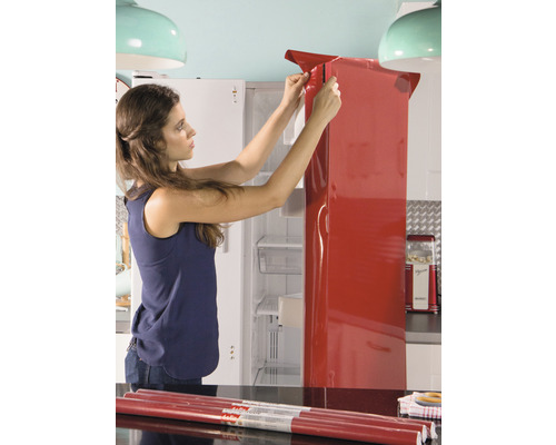 Vrouw beplakt koelkast met rode decoratiefolie in keuken.