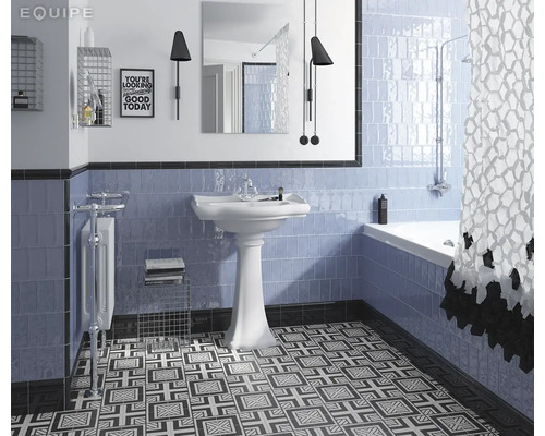 Badkamer met blauw betegelde wand, wastafel, bad en een vloer met motief.