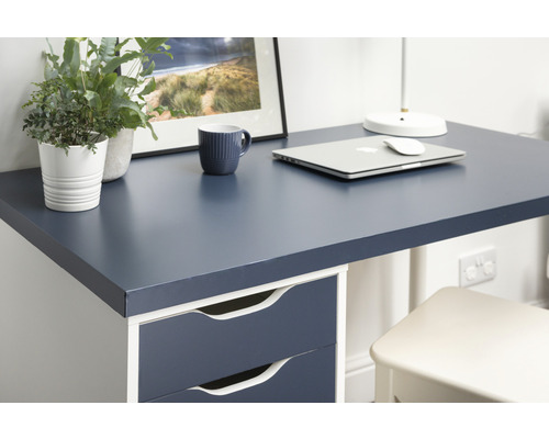 Gedetailleerde weergave van een bureau met donkerblauw blad, laden, laptop, beker en decoratie