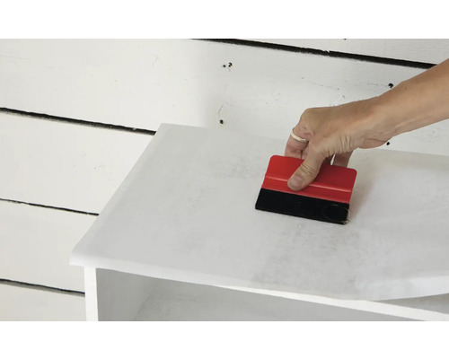 Aanbrengen van meubelfolie met een rakel op een meubelstuk.