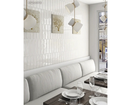 Interieurbeeld met witte, langwerpige wandtegels, een bank met kussens en gedekte tafels