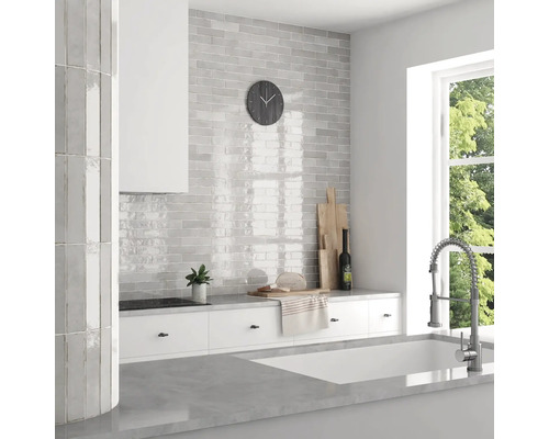 Lichte keuken met grijze tegels in baksteenpatroon, witte kasten en een raam met uitzicht op groen