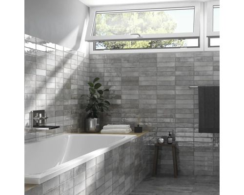 Badkamer met ligbad, wastafelarmatuur, ramen en grijze wandtegels