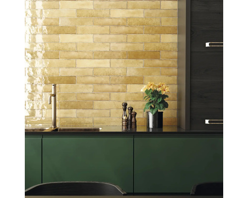 Keukenscène met gele tegels, gootsteen, kraan, kruidenmolen en potplant.