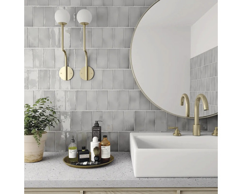 Moderne badkamer met grijze tegels, ronde spiegel, wastafel en gouden kranen