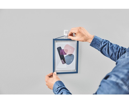 Persoon hangt ingelijste foto met zelfklevende strips aan de muur