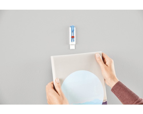 Iemand hangt met een zelfklevende fotolijsthaak een foto aan de muur.