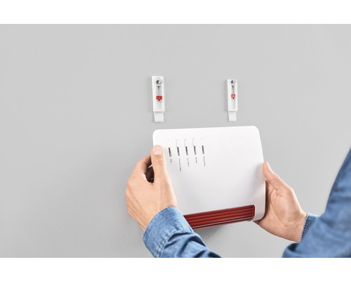 Persoon bevestigt een Fritzbox met twee zelfklevende spijkers aan de muur.