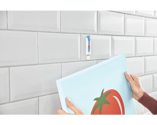 Persoon hangt foto op tegels met een plakstrip