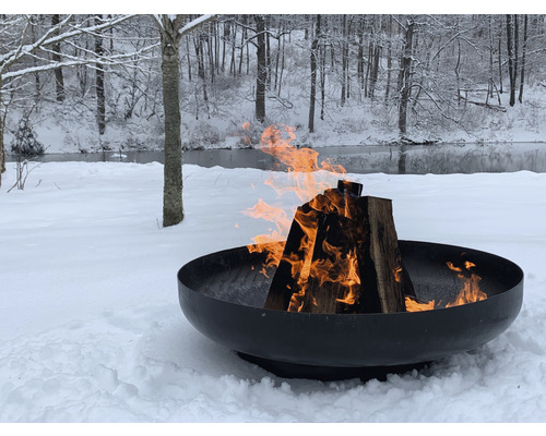 Vuurschaal met brandend hout in een besneeuwde tuin