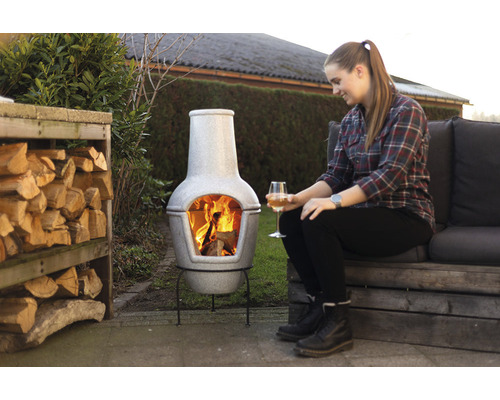 Tuinscene met chiminea-kachel, brandend hout en een vrouw met een drankje