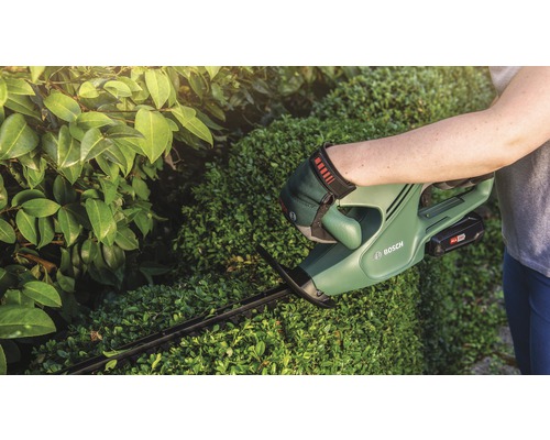 Een persoon snoeit een haag met een Bosch accu-heggenschaar.