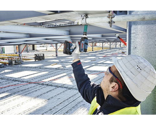 Een bouwvakker monteert met een accuschroevendraaier een pijpbevestiging aan een metalen constructie.