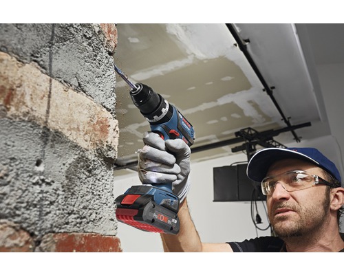 Een man boort met een accuboormachine in een bakstenen muur.