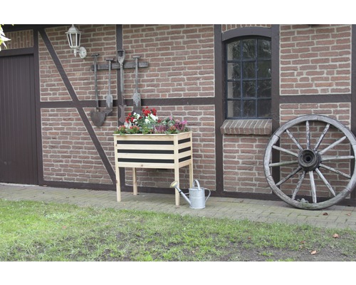 Houten bloembak met bloemen, gieter en wagenwiel voor een bakstenen gebouw