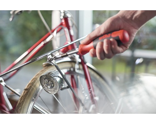 Iemand bevestigt met een schroevendraaier de lamp aan een fiets.