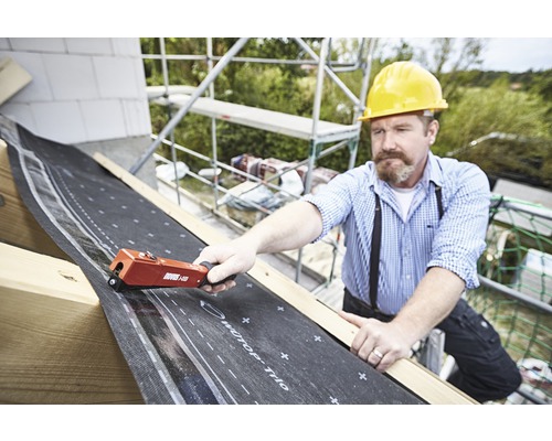 Een vakman bevestigt een dakbedekking met een handtacker op een dak.