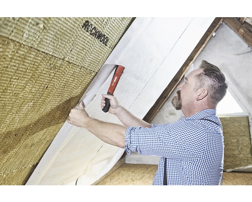 Een man bevestigt isolatiewol met een dampremmende folie aan een hellend dak.