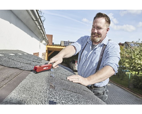 Een man bevestigt bitumineuze dakspanen met een dakleer nietmachine op een dak.