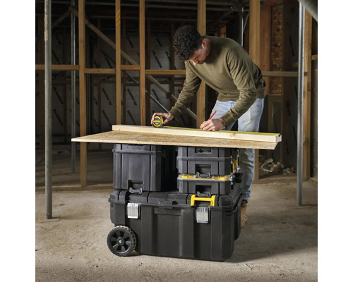 Man meet een houten plank met een rolmaat op een gereedschapskist