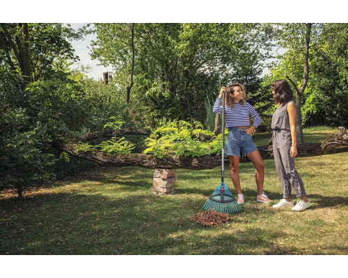Twee vrouwen staan met een hark in de tuin. Op het gazon ligt een verzameling bladeren.
