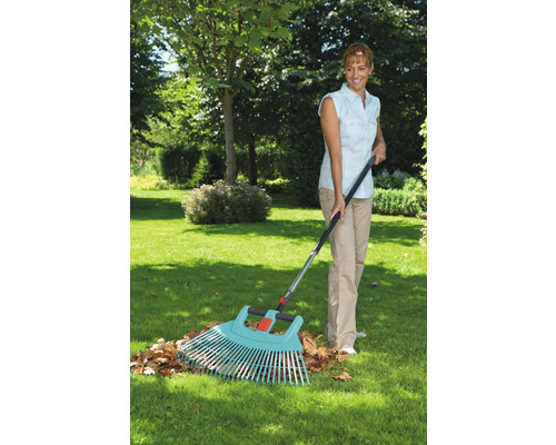 Vrouw harkt bladeren met een bladhark in de tuin.