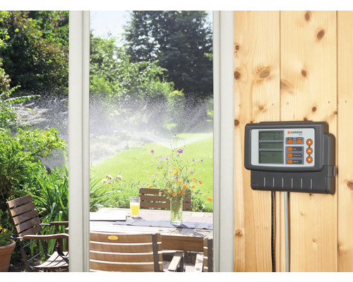 Gardena irrigatiecomputer aan een houten wand, op de achtergrond een terras en een gazonsproeier