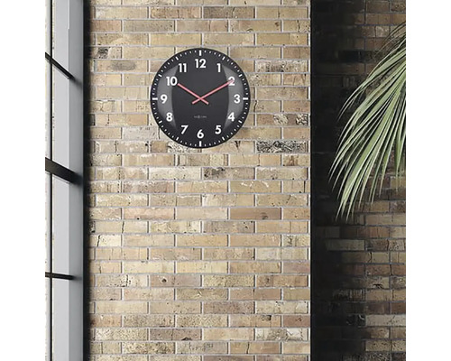 Zwarte wandklok met rode wijzers voor een bakstenen muur