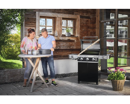 Buitenscène met een stel dat grilt naast een houtskoolgrill, met bijzettafel en houten wand
