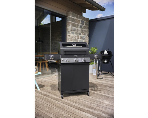 Zwarte gasbarbecue met onderkast en zijbrander op een terras.