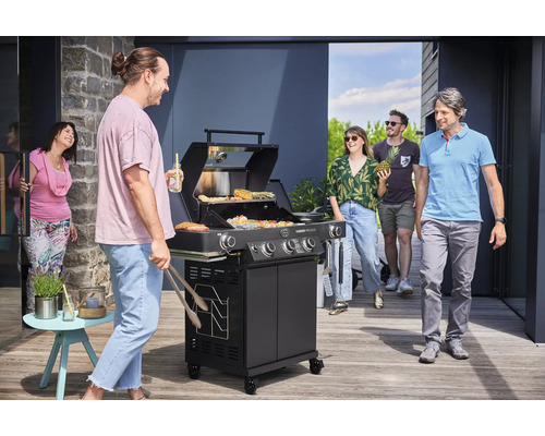 Buitenscène met een zwarte gasbarbecue, omringd door een groep mensen die aan het praten zijn en van het barbecueën genieten.