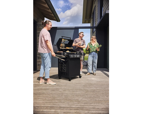Drie personen staan rond een gasbarbecue en grillen buiten.
