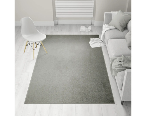 Inrichtingsvoorbeeld met grijs tapijt, stoel en bank in een lichte kamer.