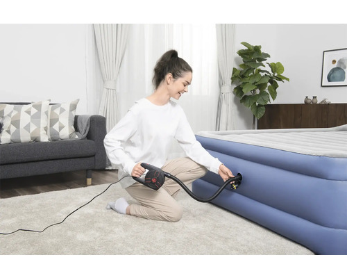 Vrouw pompt luchtmatras op met een elektrische pomp in een heldere woonkamer