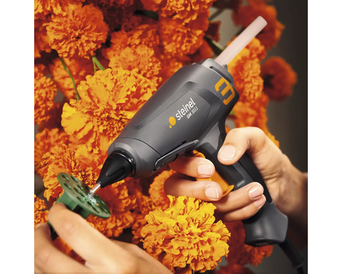 Steinel lijmpistool dat een werkstuk vastlijmt met smeltlijm voor een achtergrond van oranje bloemen.