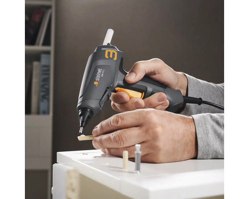 Een persoon gebruikt een Steinel lijmpistool om stukken hout op een wit oppervlak te lijmen.