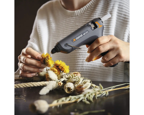 Persoon bevestigt bloemen op een krans met een lijmpistool