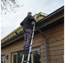 Man reinigt dakgoot met een telescoopladder aan een huis.
