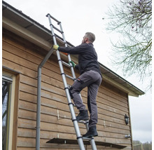 Een persoon beklimt een telescopische ladder tegen een huismuur.