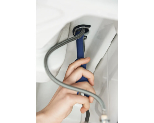 Een vakman installeert een kraan met gereedschap en een flexibele slang.