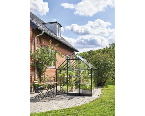 Glazen kas met stalen frame naast een woonhuis met tafel en stoelen op een terras