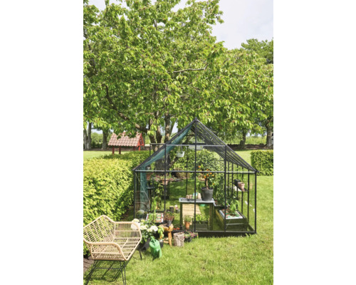Glazen en metalen serre in de tuin met planten en tuinaccessoires