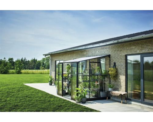 Glazen en metalen kas aan een bakstenen gebouw met planten en tuinmeubilair
